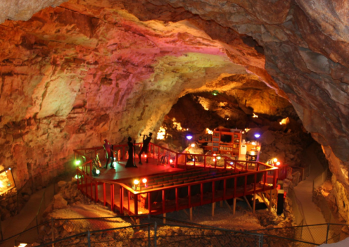 A colorful cave interior with a wooden platform, lights, and figures, showcasing a unique underground setting.