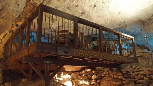 A wooden platform with chairs and tables inside a cave, illuminated by soft blue lighting.