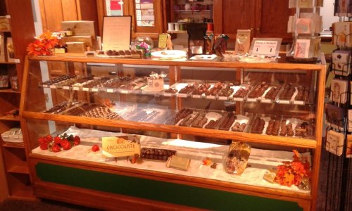 A display case filled with various chocolates, decorated with autumn leaves and signs in a cozy shop setting.