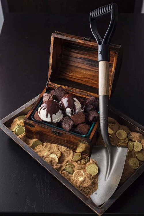 A treasure chest filled with ice cream, brownies, and chocolate sauce, surrounded by gold coins and a shovel.