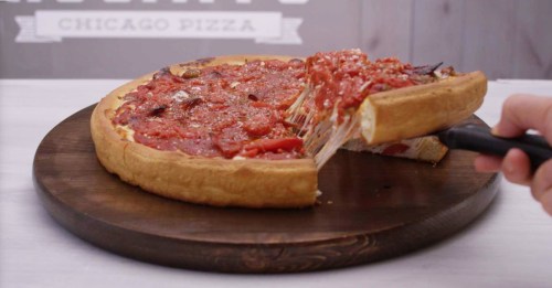 A slice of Chicago-style pizza being lifted from a round pizza on a wooden board, topped with tomato sauce and cheese.