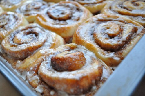 A close-up of freshly baked cinnamon rolls drizzled with icing in a baking pan.