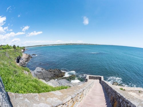 A scenic view of a rocky coastline with steps leading down to the water, under a clear blue sky.