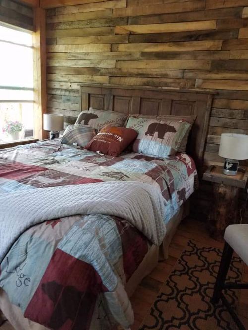 Cozy bedroom with a wooden accent wall, a bed with a patterned quilt, and bedside lamps on rustic tables.