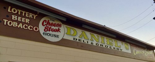 Sign for Daniel's Deli & Grocery featuring The Cheese Steak House, with listings for lottery, beer, and tobacco.