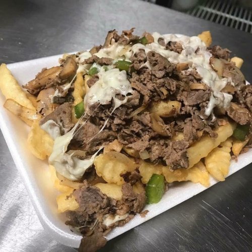 A plate of loaded fries topped with seasoned beef, sautéed mushrooms, green peppers, and melted cheese.
