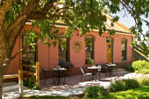 A charming restaurant exterior with outdoor seating, surrounded by greenery and a tree, featuring a warm, inviting atmosphere.
