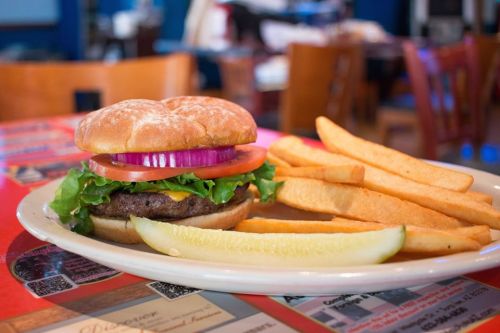 A juicy hamburger with lettuce, tomato, onion, and cheese, served with golden fries and a pickle on a plate.