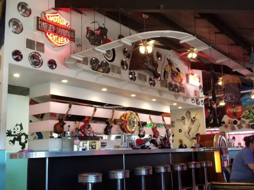A retro diner interior featuring a bar with stools, motorcycle decor, and vintage memorabilia on the walls.