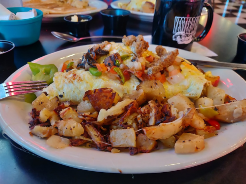 A hearty breakfast plate featuring a large omelet with vegetables, sausage, and crispy potatoes on the side.