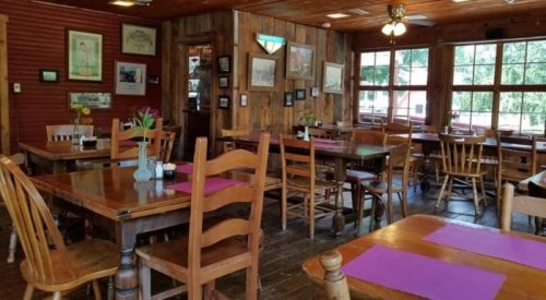 Cozy restaurant interior with wooden tables, chairs, and large windows, featuring rustic decor and purple table settings.