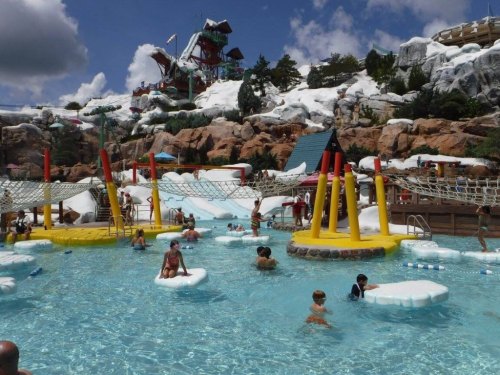 A vibrant water park scene with children playing in a pool, surrounded by slides and rocky, snowy decor.