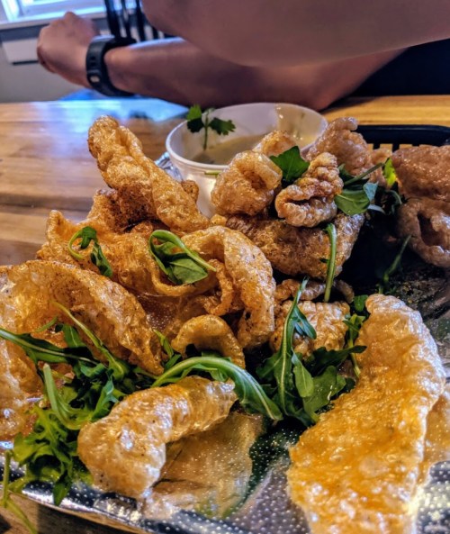 A plate of crispy pork rinds garnished with fresh greens and a small bowl of dipping sauce.