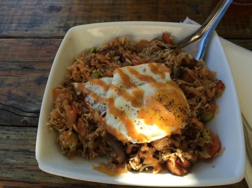 A bowl of rice topped with a poached egg and drizzled with sauce, served on a wooden table.
