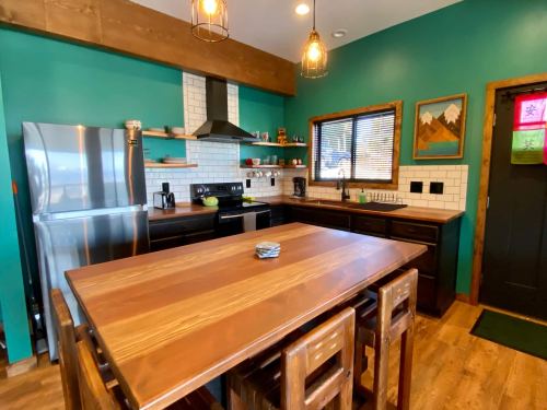 Modern kitchen with teal walls, wooden accents, stainless steel appliances, and a large wooden dining table.