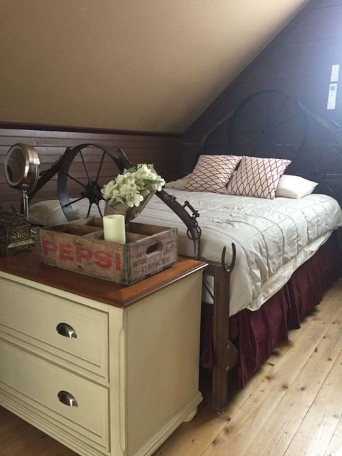 Cozy attic bedroom with a bed, decorative pillows, a vintage nightstand, and rustic decor elements.