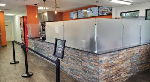 A modern restaurant interior with a service counter, frosted glass partitions, and a sign directing customers to enter.