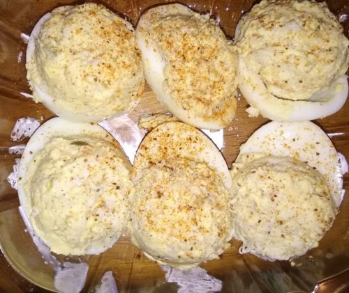 A close-up of six stuffed deviled eggs topped with seasoning, arranged in a glass dish.