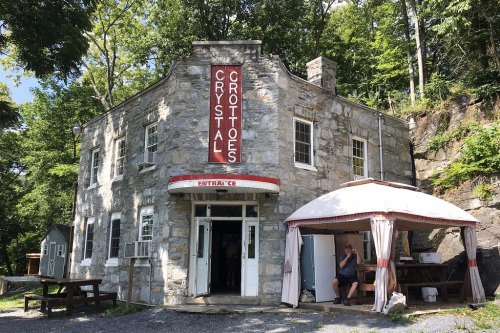 A stone building with a sign reading "Crystal Grottoes," surrounded by trees and featuring an outdoor seating area.