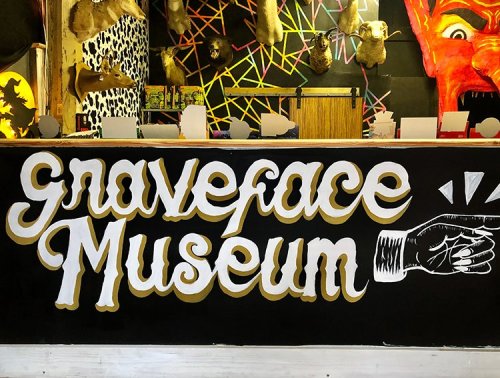 A colorful mural featuring the text "Graveface Museum" with artistic designs and mounted animal heads in the background.