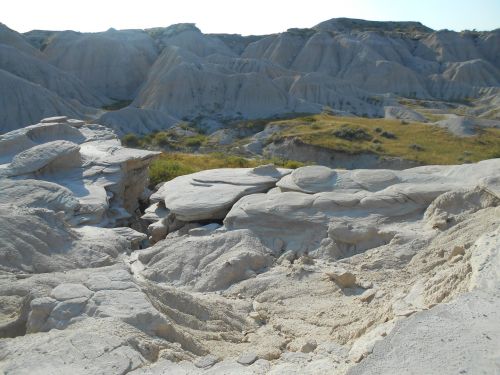 A rocky landscape with smooth, layered formations and sparse vegetation under a clear sky.