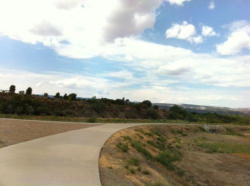 A winding concrete path leads through a grassy area under a partly cloudy sky with distant hills in the background.