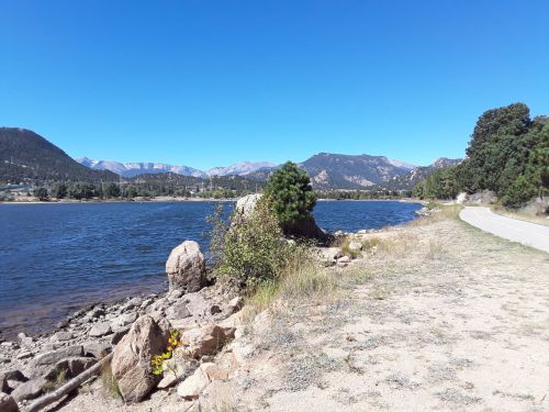 Scenic view of a lake surrounded by mountains, with a clear blue sky and a path along the water's edge.
