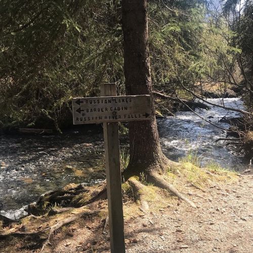Wooden signpost with arrows pointing to Russian Lakes, Barber Cabin, and Russian River Falls, beside a flowing stream.