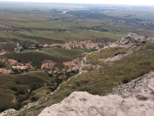 A panoramic view of rolling green hills and rugged terrain under a cloudy sky.