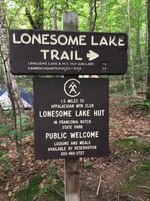 Sign for Lonesome Lake Trail, indicating distance to Appalachian Mountain Club hut and public welcome for lodging and meals.