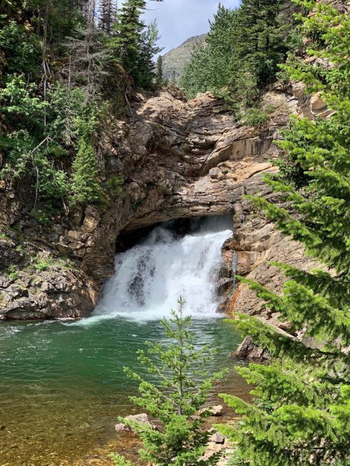 A serene waterfall cascades into a clear pool, surrounded by lush greenery and rocky cliffs.