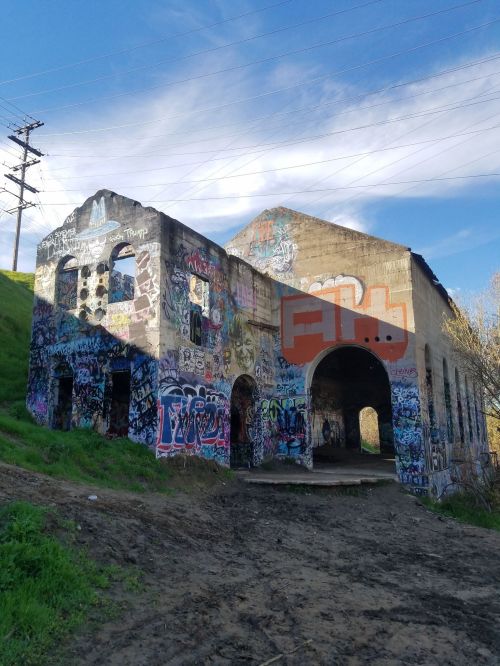 Abandoned building covered in colorful graffiti, set against a blue sky and green hillside.