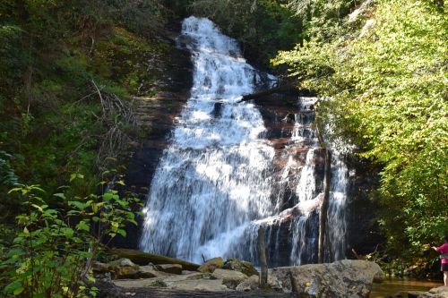 A cascading waterfall surrounded by lush greenery and rocks, with a person standing nearby.