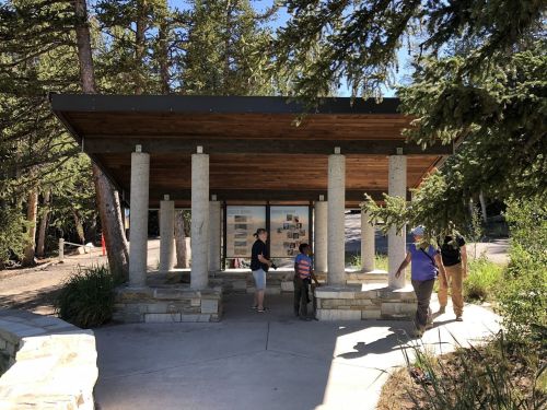 A modern pavilion with stone columns, surrounded by trees, where people are exploring informational displays.