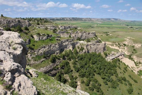 A panoramic view of rugged cliffs and green valleys under a blue sky with scattered clouds.