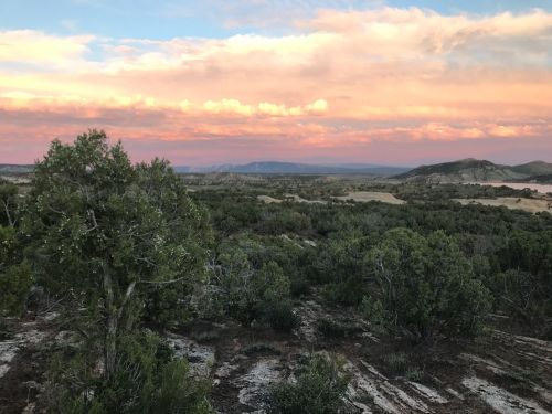 A scenic landscape featuring rolling hills, green vegetation, and a colorful sunset sky with clouds.