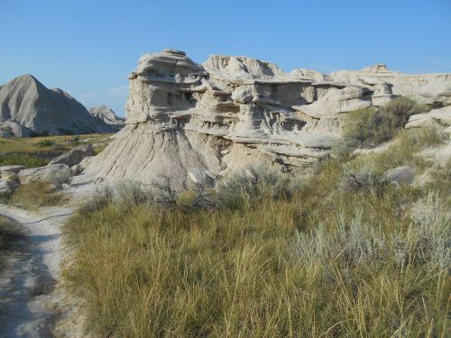 Rocky formations and grassy terrain under a clear blue sky in a desert landscape.