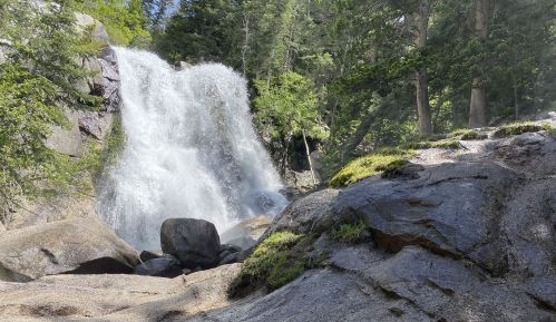 A cascading waterfall surrounded by lush greenery and rocky terrain under a clear blue sky.