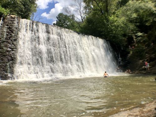 A waterfall cascades into a serene pool, with people enjoying the water and lush greenery surrounding the scene.
