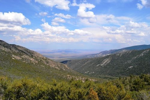 A panoramic view of a valley surrounded by mountains under a blue sky with fluffy white clouds.