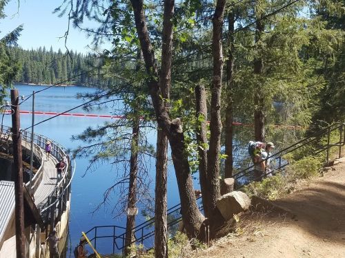 A serene lake surrounded by trees, with people walking along a path and stairs leading down to the water.