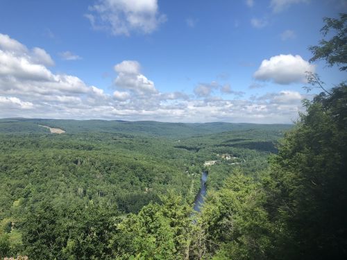 A panoramic view of lush green hills and a winding river under a partly cloudy sky.