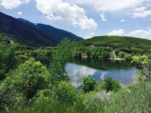 A serene landscape featuring a calm lake surrounded by lush greenery and mountains under a partly cloudy sky.