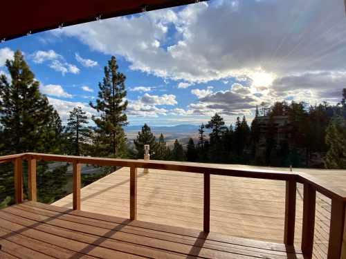 A scenic view from a wooden deck overlooking a valley, with trees and clouds under a bright sky.