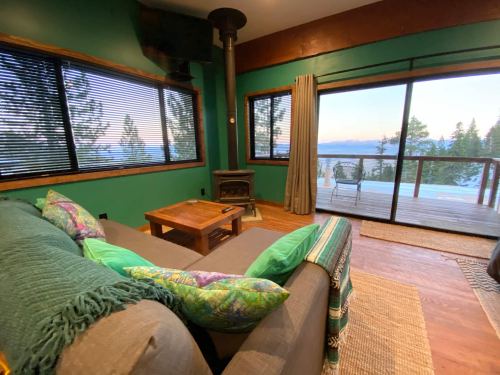 Cozy living room with a green wall, a sofa, a wooden table, and a view of trees and mountains through large windows.