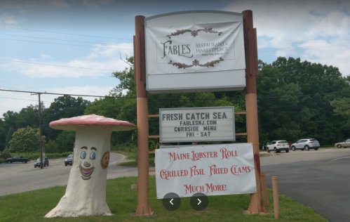 Sign for Fables Restaurant featuring a smiling mushroom and menu items like lobster rolls and fried clams.