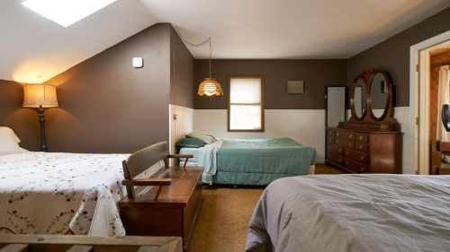 Cozy bedroom with two beds, a dresser, and a lamp, featuring warm tones and natural light from a skylight.