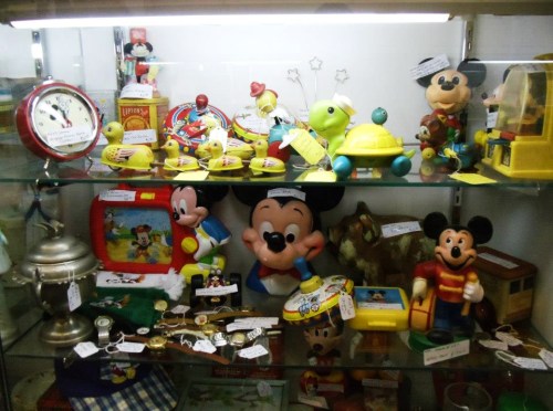 A display case filled with vintage Mickey Mouse toys, clocks, and collectibles, all labeled with price tags.