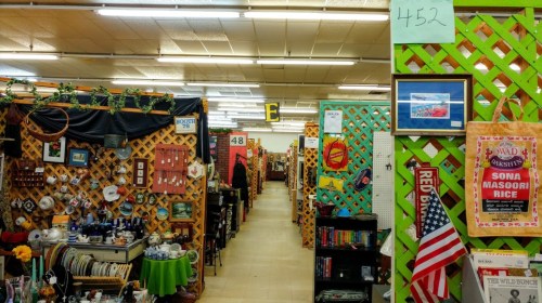 A colorful aisle in a thrift store, lined with booths displaying various items and decorations.