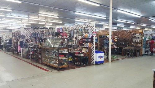 A spacious antique shop filled with various collectibles, displays, and merchandise under bright fluorescent lights.